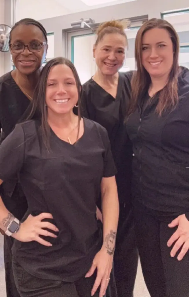 Four women in black scrubs smiling together.