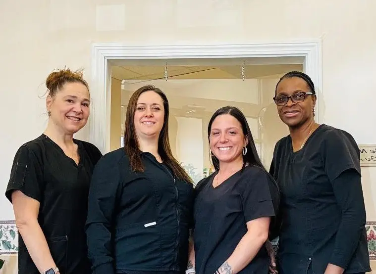 Four women in black scrubs smiling together.